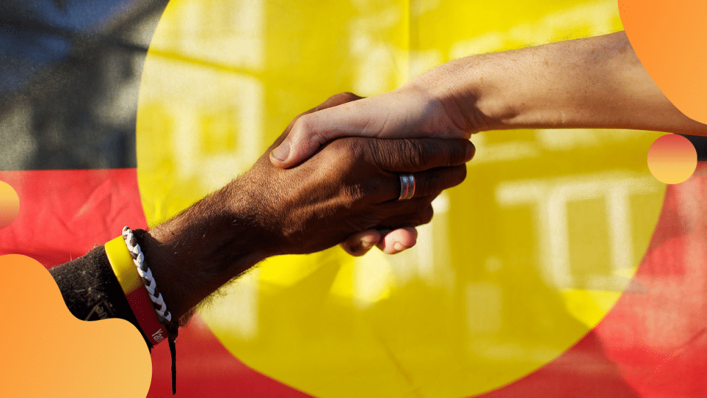Black and white hands joined in front of the Aboriginal flag