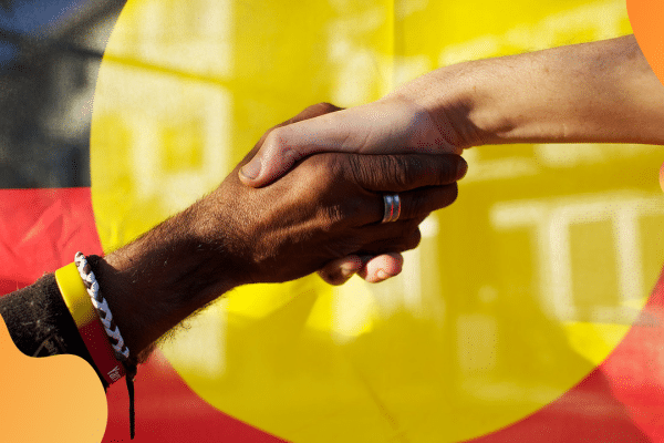 Black and white hands joined in front of the Aboriginal flag