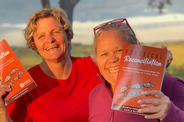 Carla Rogers and Aunty Munya Andrews holding up their book Practical Reconciliation