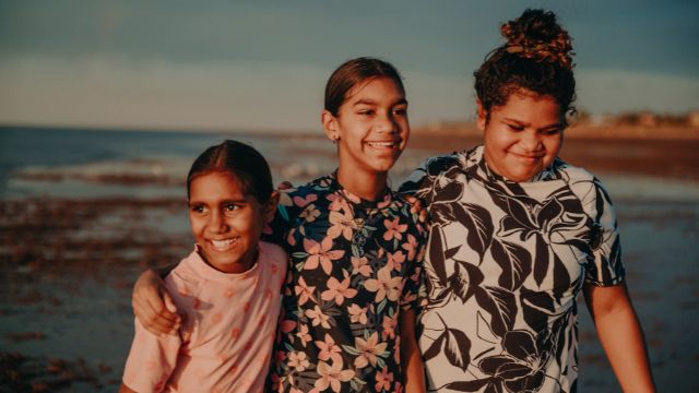 Three Aboriginal girls walking along the beach, arm in arm and smiling - Evolve Close The gap Report 2024